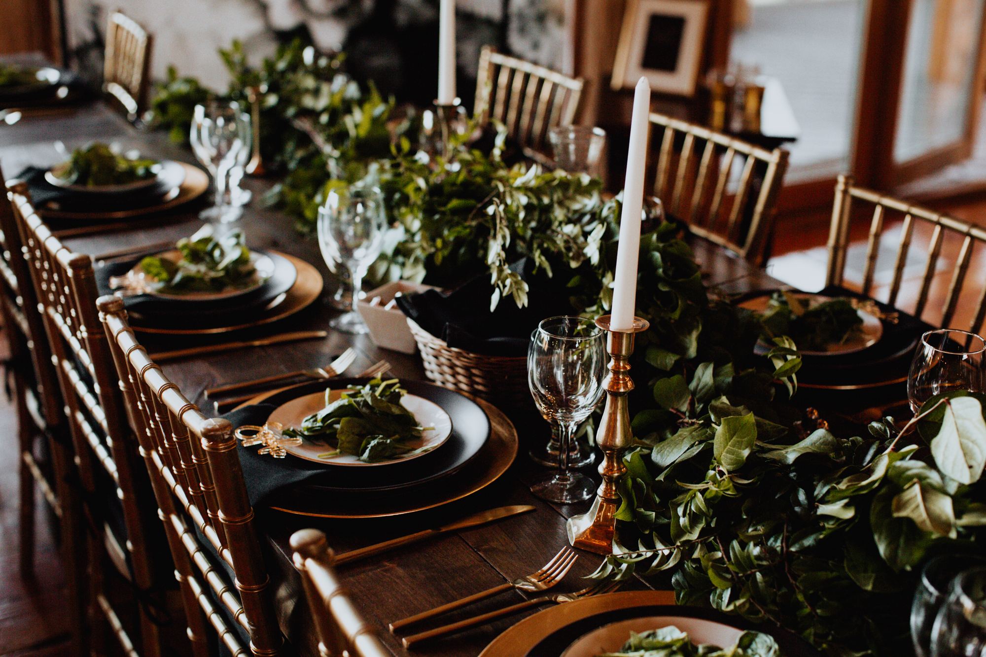 Place settings, taper candles, and trailing greenery on a dark wood table